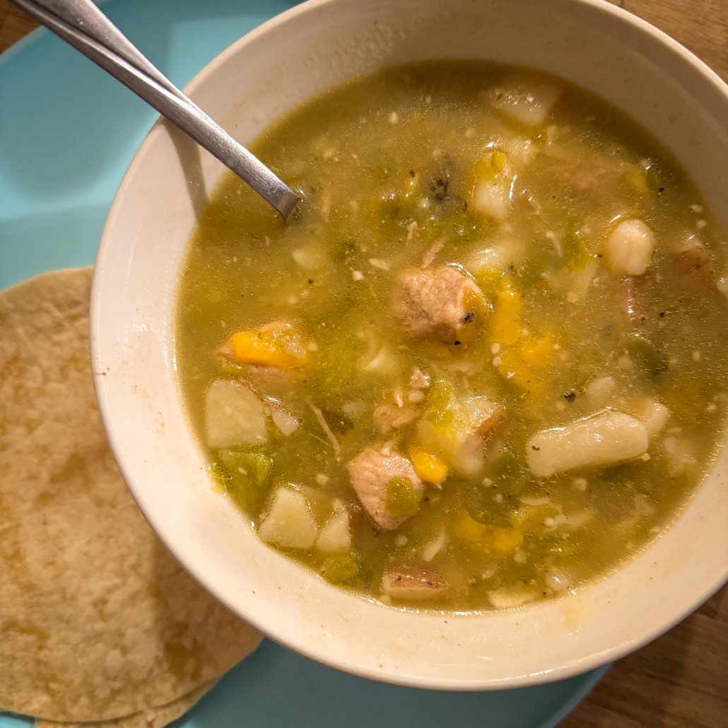 Bowl of green chile stew with corn tortillas.